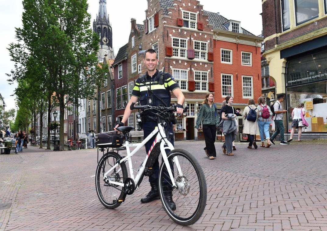 Cornelius staat in uniform met zijn fiets in de hand in de Delftse binnenstad