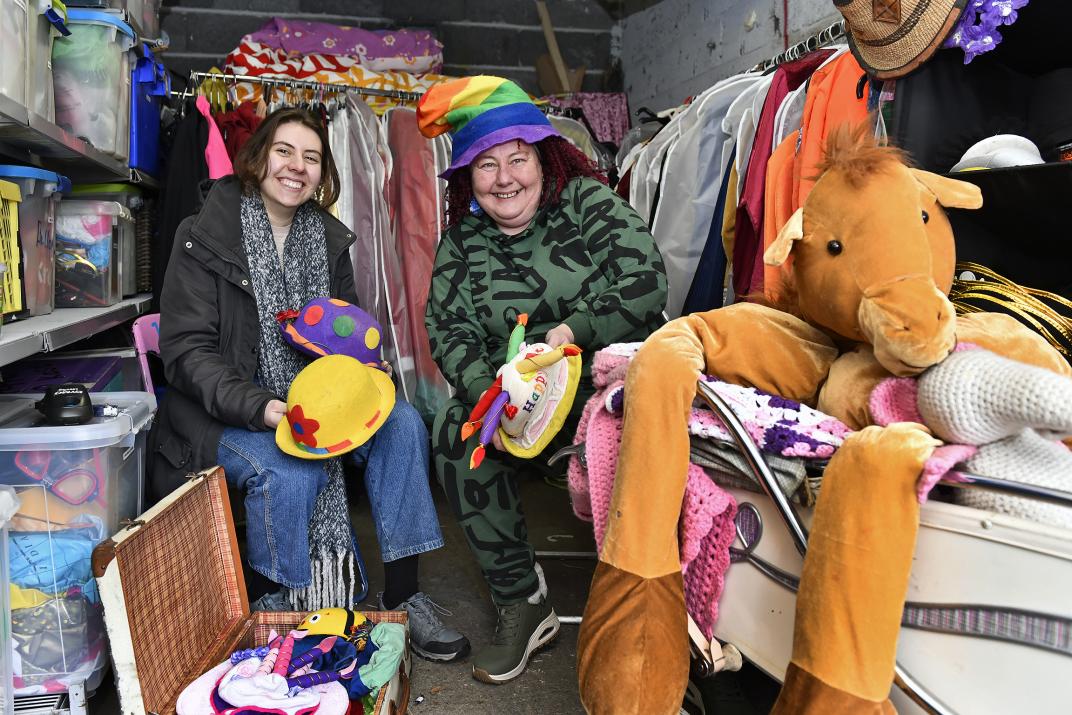 Ugne en Myrrhe in een van de garageboxen van de Clowniek Fabriek. Op de achtergrond zijn rekken met kleurrijke kleding en andere clownspullen te zien.